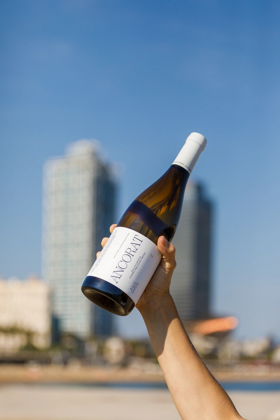Mujer sujetando botella de vino ancorat con torres mafre de fondo y skyline de barcelona.