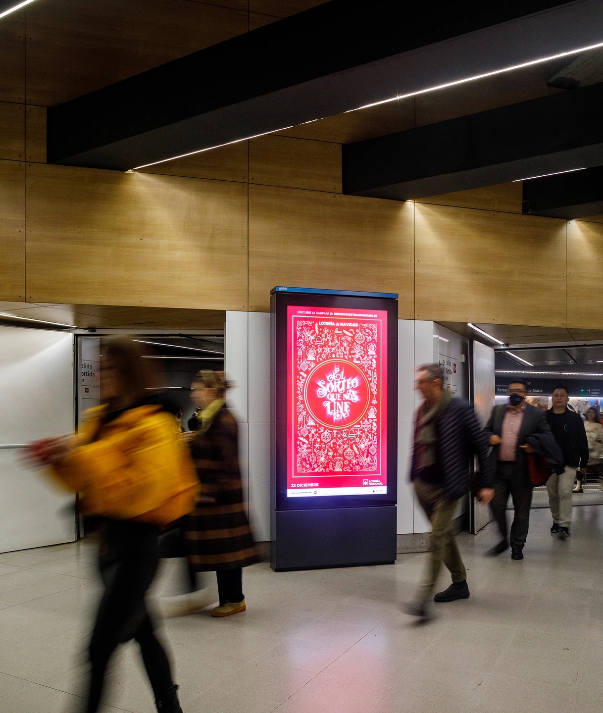 Gente pasando desenfocada delante de un Mupi digital del metro de paseo de gracia