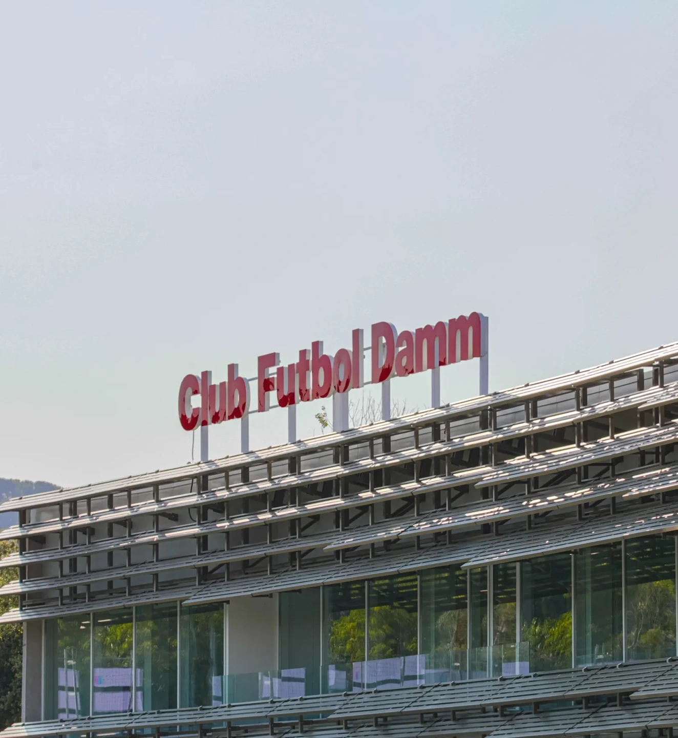 Club de futbol Damm en Montjuïc, Barcelona. Logotipo en rojo con el nombre del club encima del edificio.