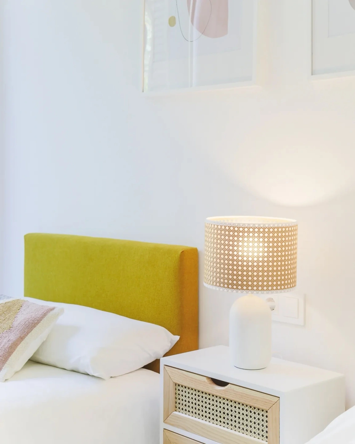 Fotografía de detalle de cabecero amarillo, mesita blanca y lámpara de fibras en un dormitorio de Atelier Apartments.