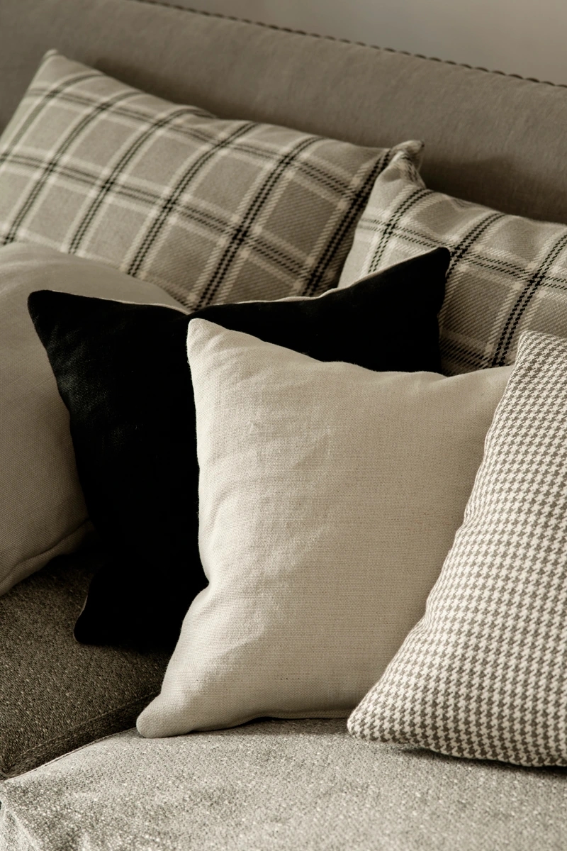 Colección Dart Moor de Les Créations de la Maison en Barcelona. Cojín con patrón de pata de gallo, otro con patrón escocés, otro de tejido liso blanco y uno de terciopelo negro,todo en gris.