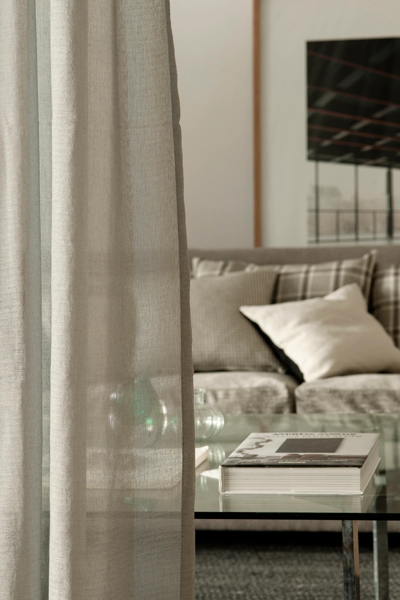 Colección Dart Moor de Les Créations de la Maison en Barcelona. Cojín con patrón de pata de gallo y otro con patrón escocés, todo en gris. En primer plano se ve una cortina de un tejido gris muy suave y de calidad premium.