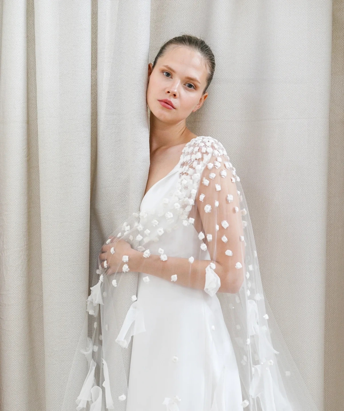 Fotografía de un vestido de novia de la colección Peter Langner con capa de tul bordada con flores en relieve, retrato medio en fondo neutro.