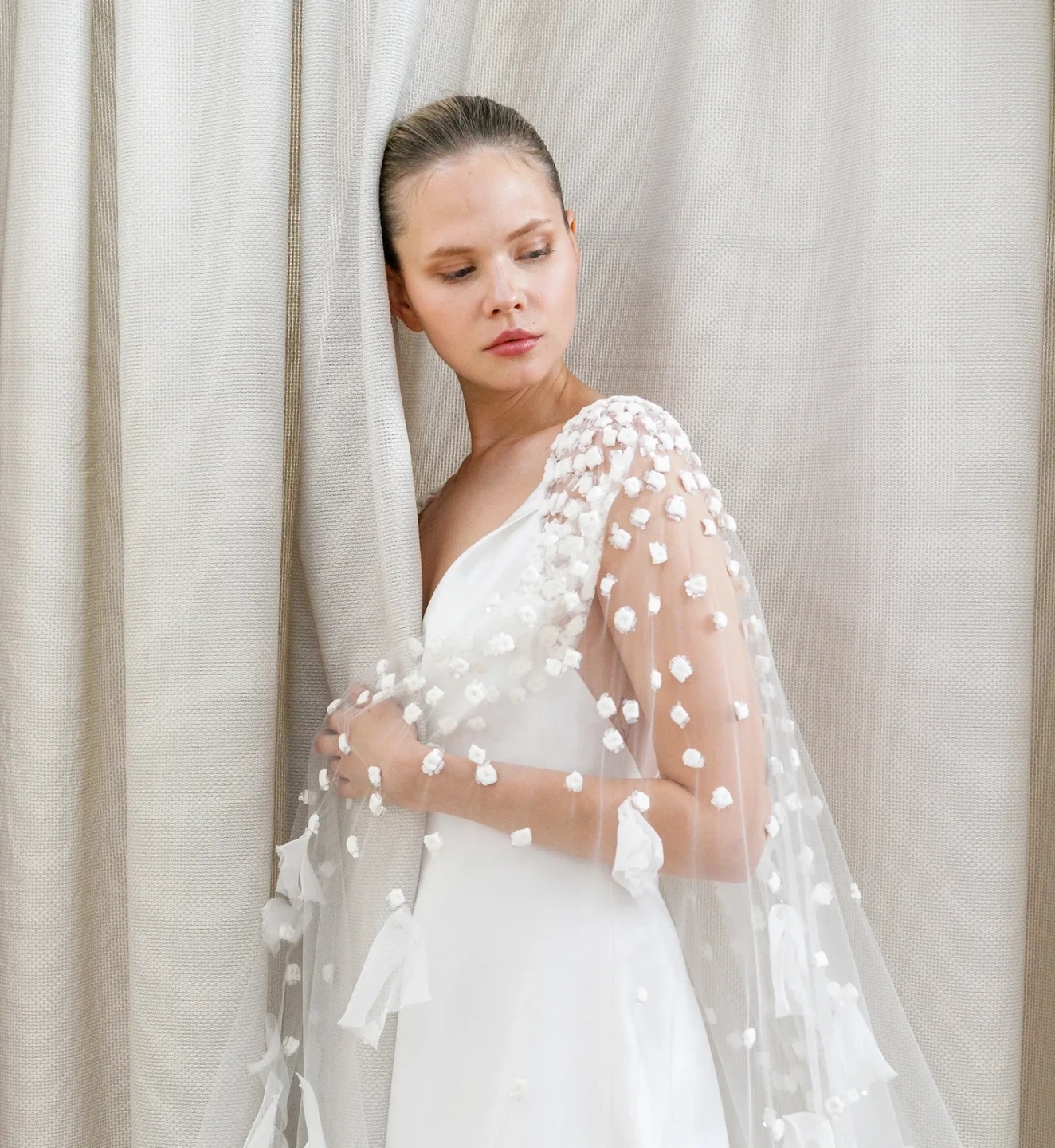 Fotografía de un vestido de novia de la colección Peter Langner, detalle lateral de la capa de tul con aplicaciones florales sobre fondo claro.