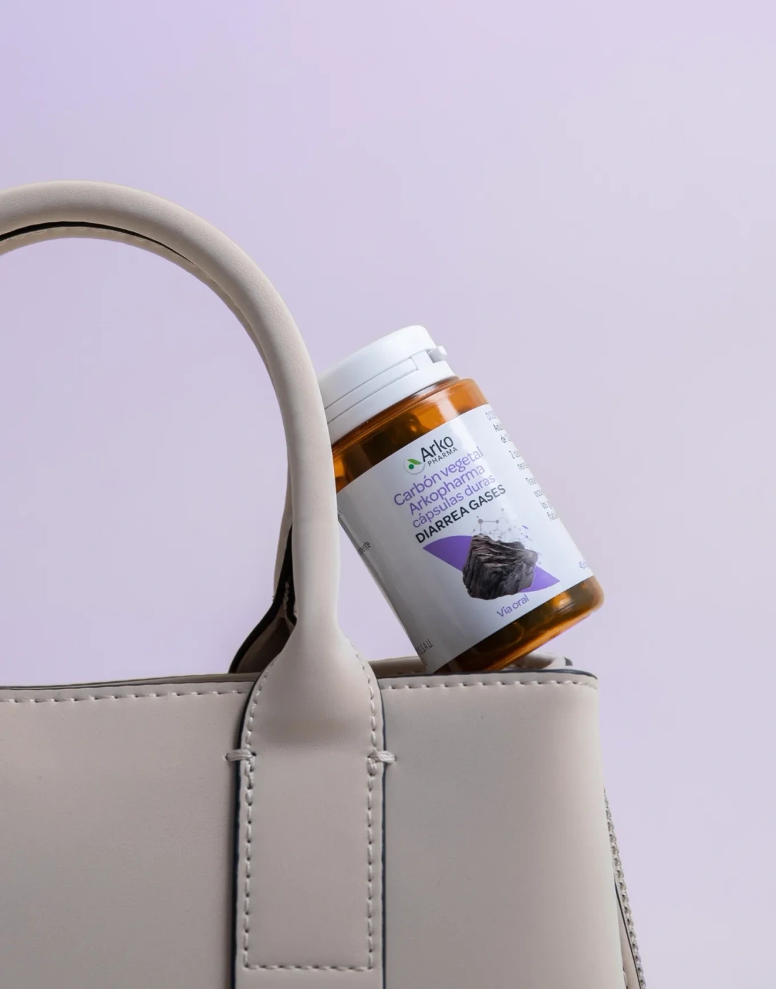 Arkocápsulas de carbón vegetal encima de un bolso beige con fondo violeta, producto de la farmacéutica Arkopharma para una sesión fotográfica creativa en Madrid.