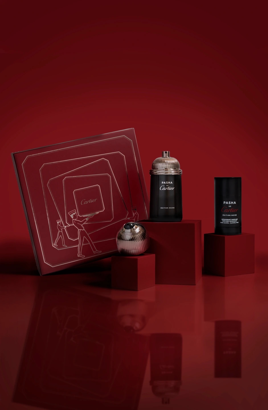Composición oscura del perfume Cartier PASHA, con el desodorante y la caja en la que viene envuelto. Fondo rojo oscuro. Fotografía para la marca de perfumerías Éclair.