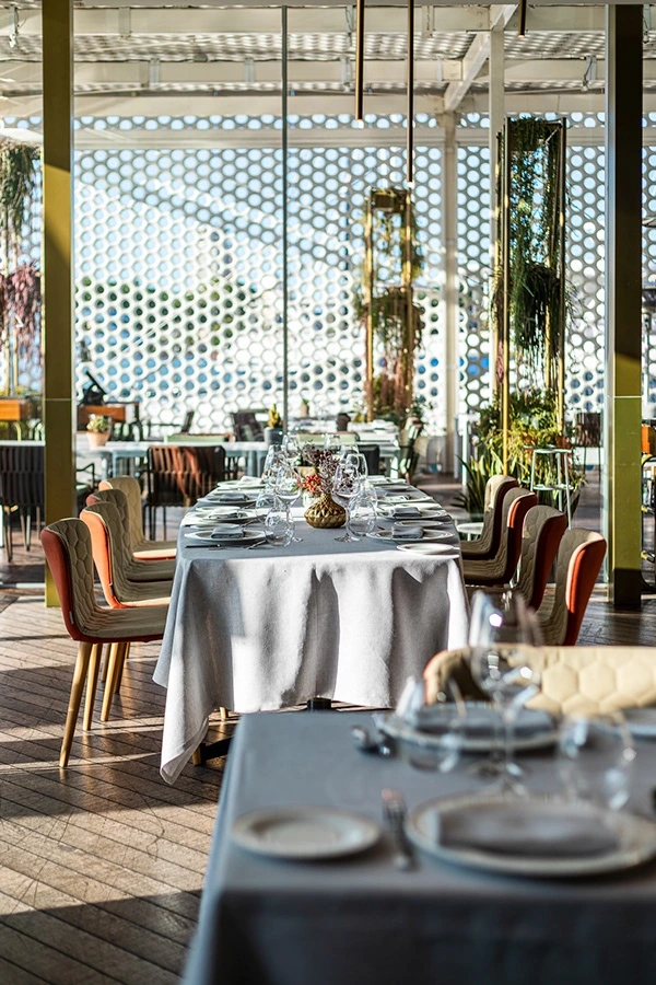 Mesa alargada preparada para un servicio con centros florales dorados y vistas al exterior.