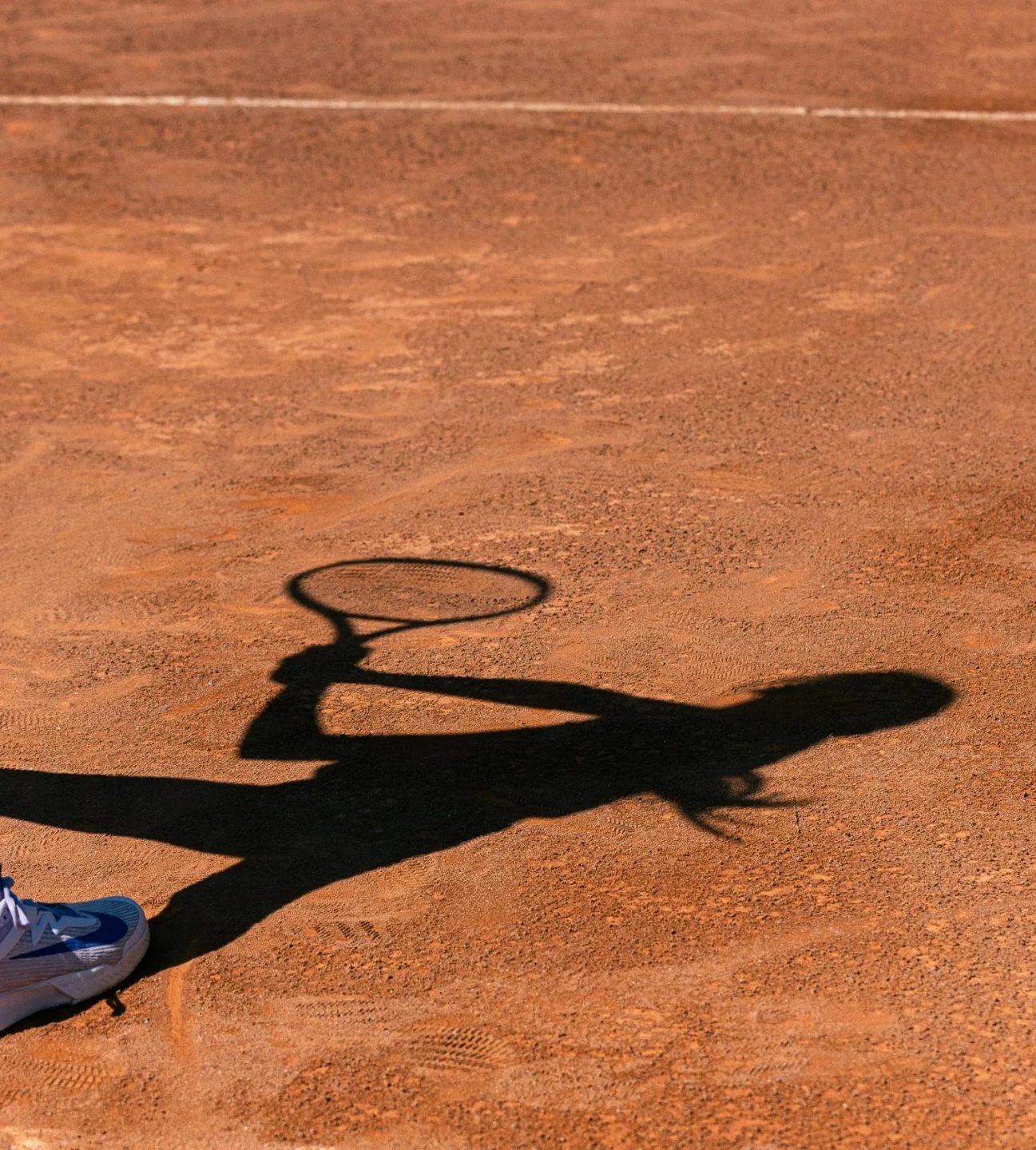 sombra de una niña adolescente jugando a tenis en una pista profesional de tierra batida con equipación de la marca ROGGIO de color azul.  