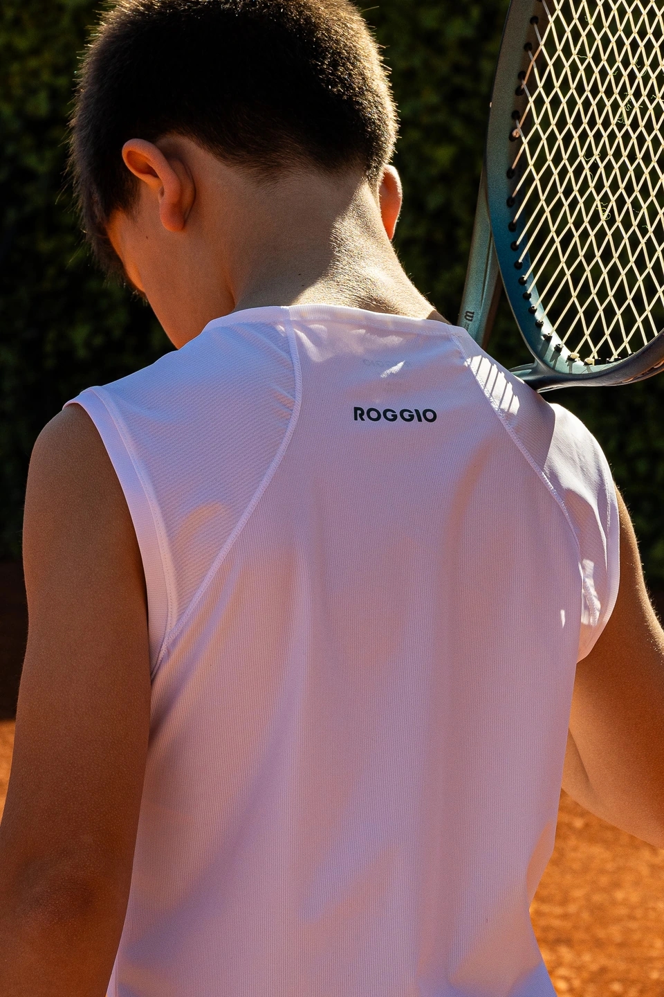 niño jugando a tenis en una pista profesional de tierra batida con equipación de la marca ROGGIO de color blanco 