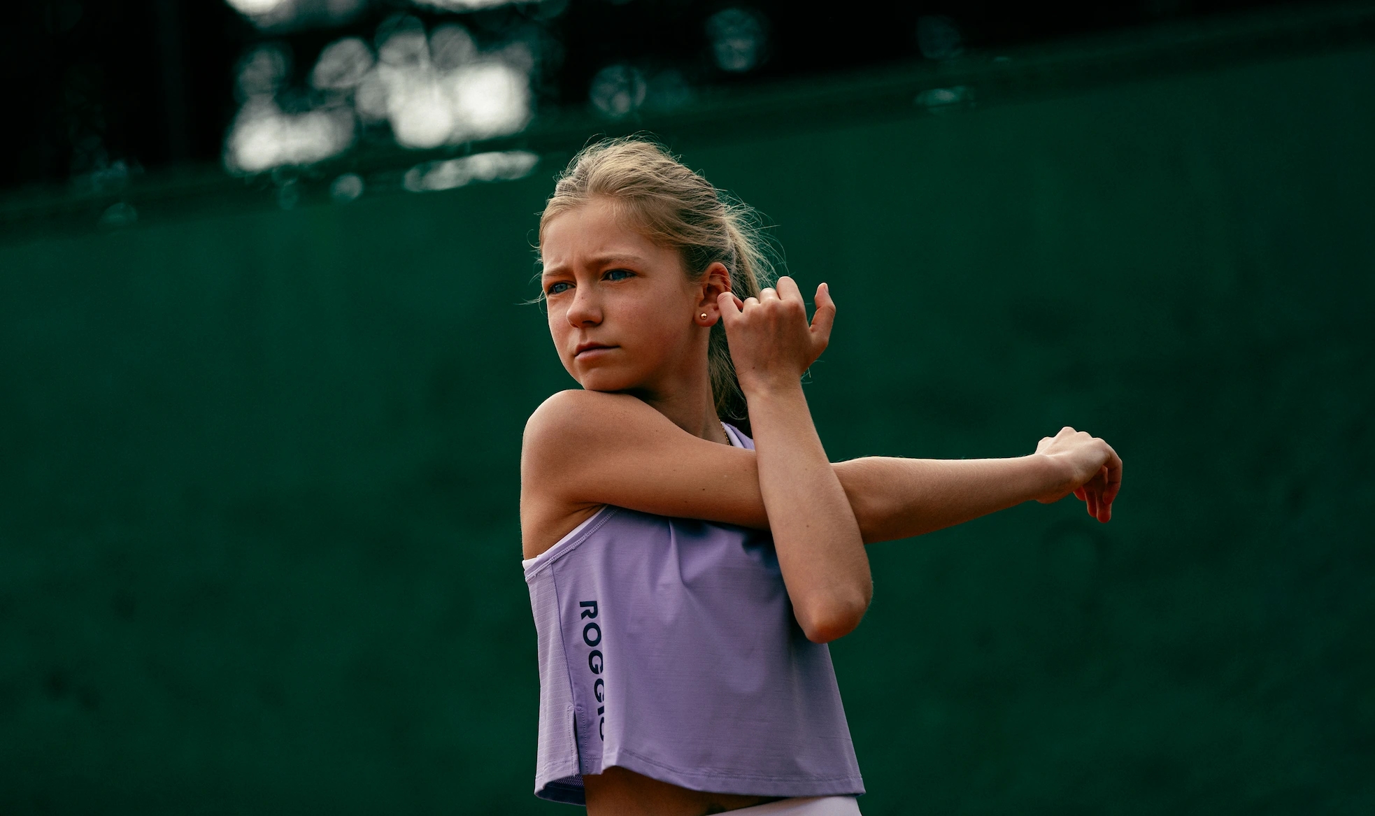 Niña de 10 años calentando en una pista de tenis con una camiseta de tirantes lila de la colección roggio