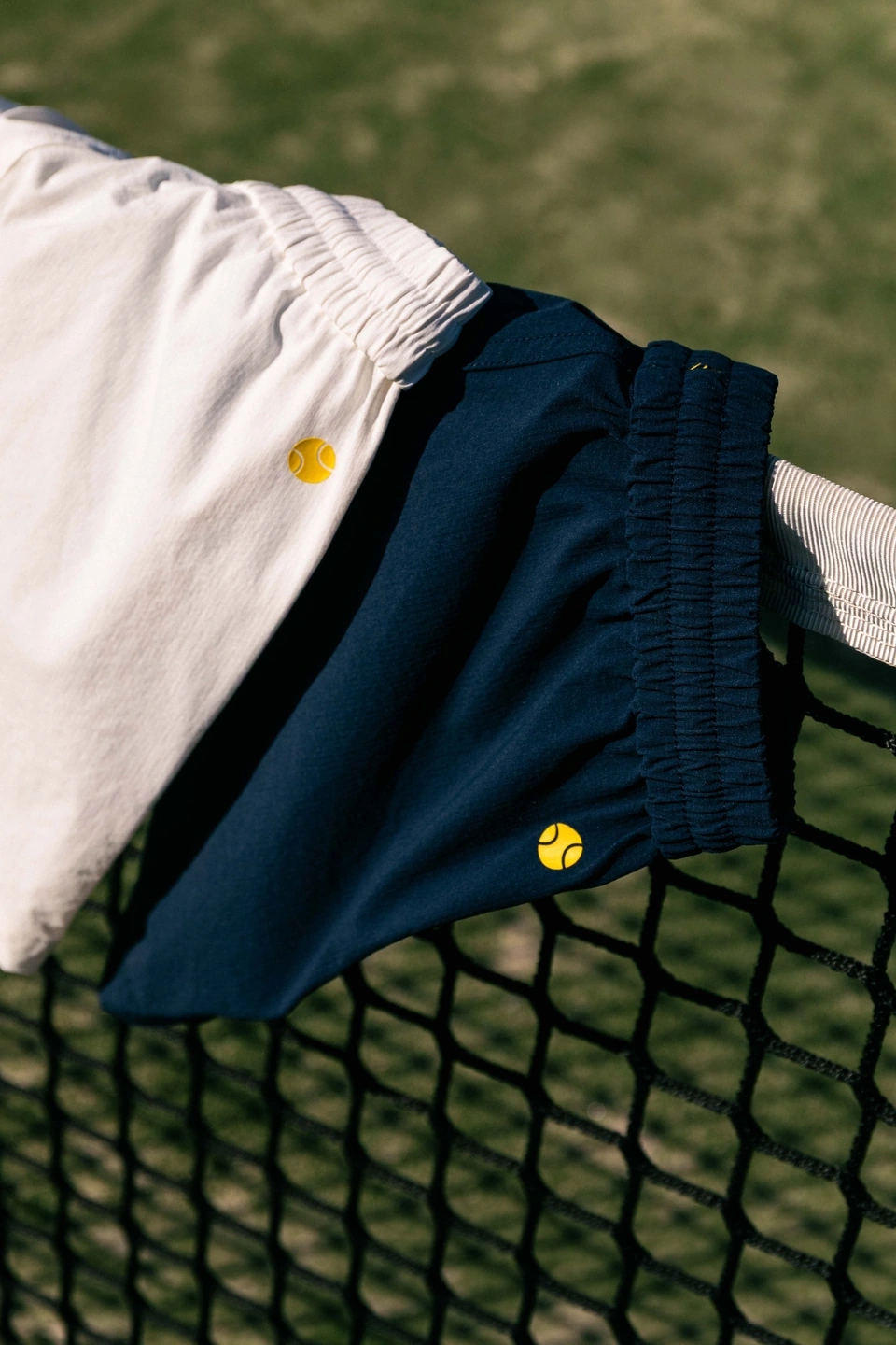 Detalles de los Pantalones azul oscuro y blanco Roggio en un campo de hierba de tenis, encima de una red de tenis.