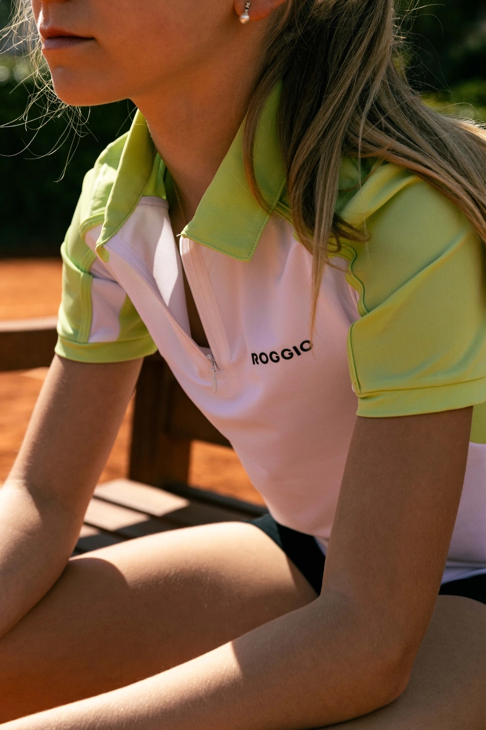 Detalle del polo Roggio blanco y verde en un niña sentada en un banco de tenis