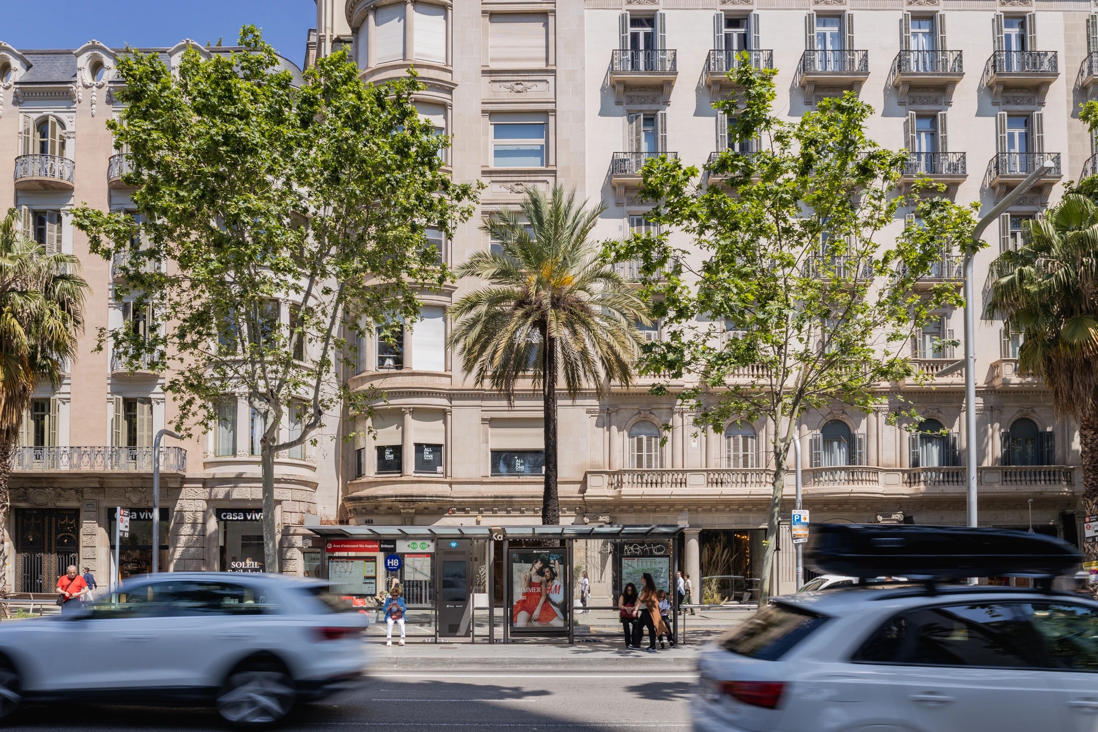 Fotografía de marquesina con cartel publicitario en Vía Augusta, Barcelona, con tráfico y peatones.