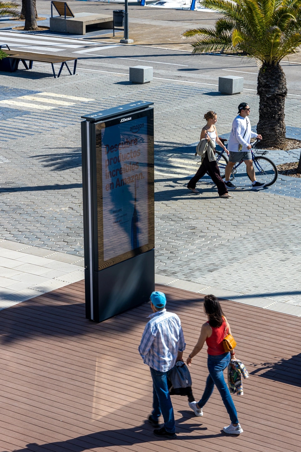 Cartel publicitario en el Port Olímpic de Barcelona con palmeras y cielo despejado.