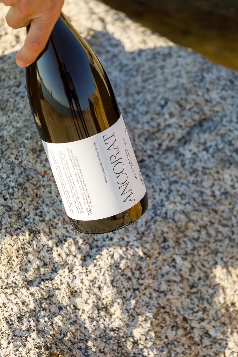 Mujer recoge dos copas de vino blanco "ancorat" de la marca Joan Sardà y la botella de vino en un espigón de barcelona con vistas al mediterráneo.