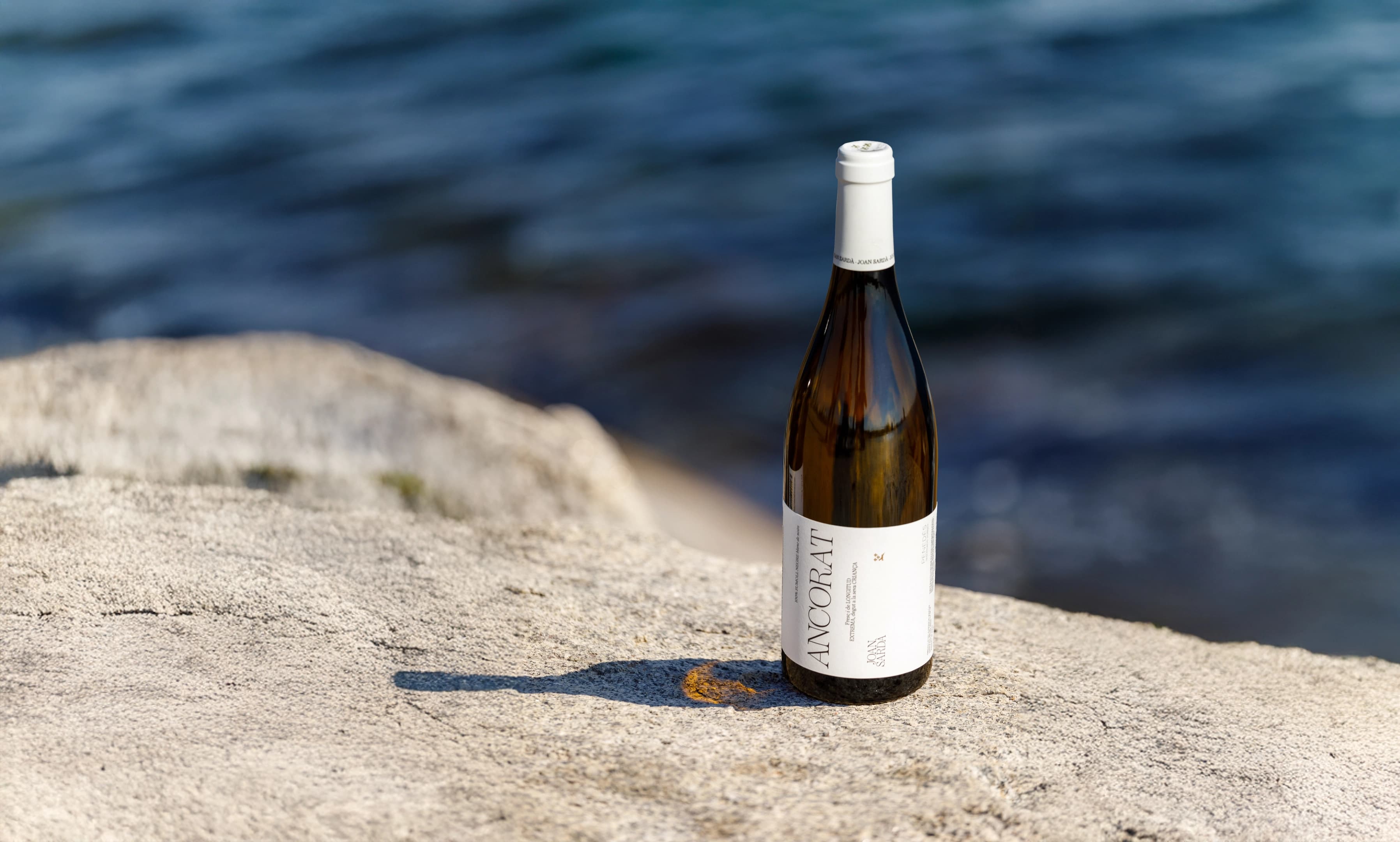 Botella de vino Ancorat en una roca con el mar Mediterráneo de fondo desenfocado.