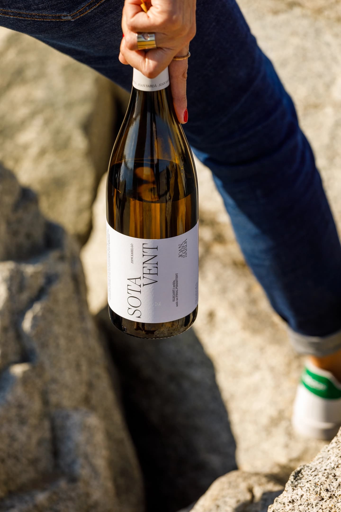 Mujer camina con un vino con nombre Ancorat, de la marca Joan Sardà  en un espigón de barcelona con vistas al mediterráneo.
