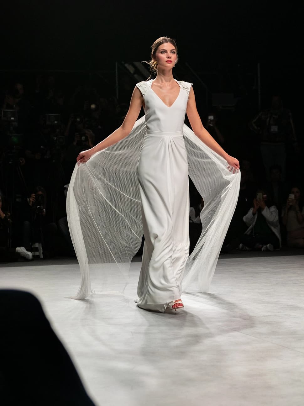 Modelo agitando el velo en forma de capa mientras anda de frente para el desfile de Beba's en la Barcelona Bridal Fashion Week.