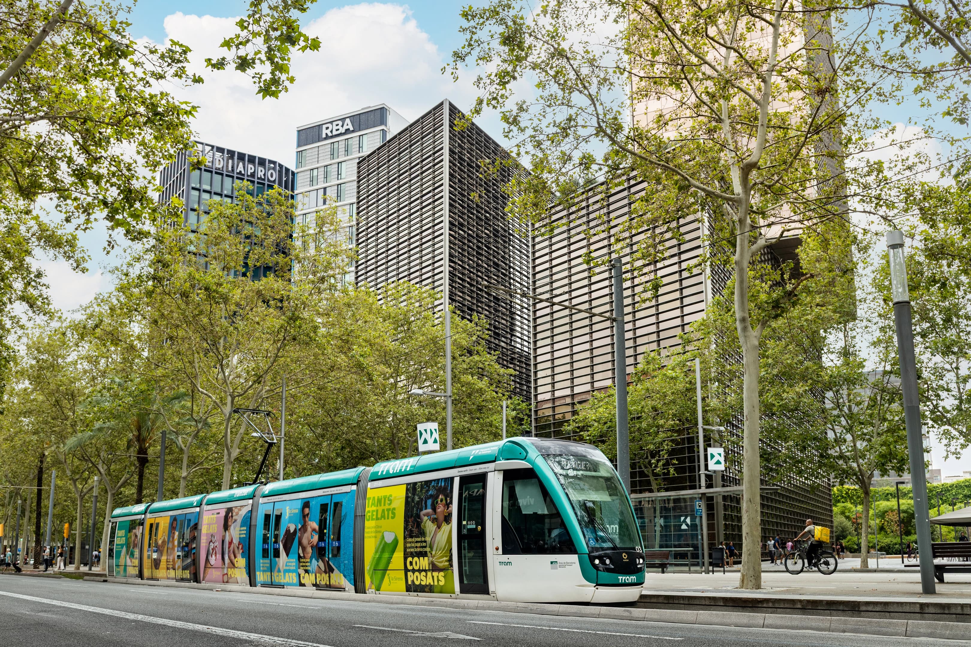 Fotografía del tranvia de Barcelona en colores blanco y verde turquesa con un fondo de edificios modernos 