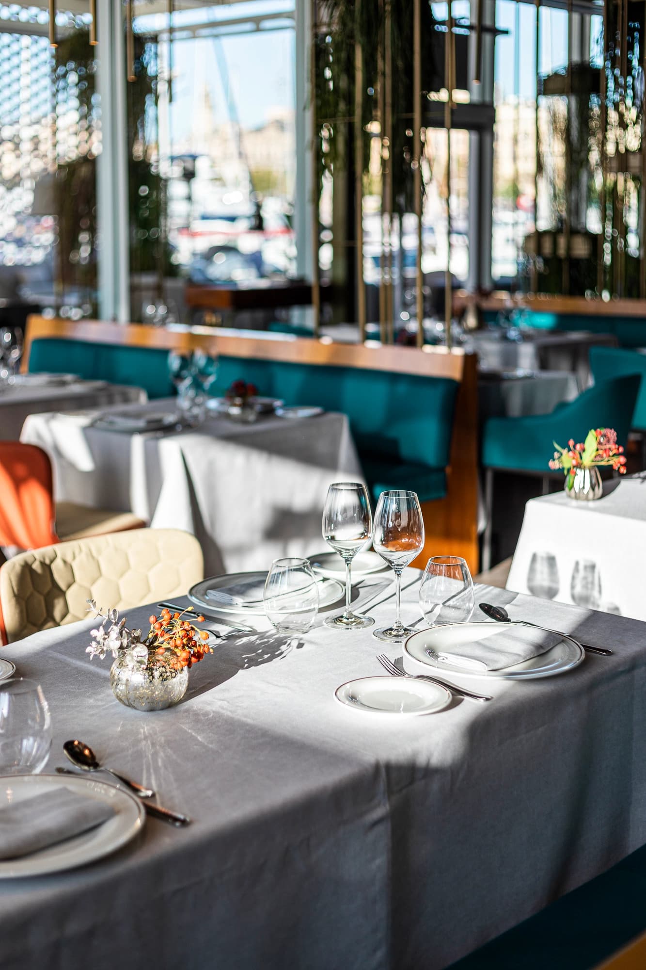 Mesa preparada en el restaurante Marina Port Vell con sillas turquesa y montaje de mesa iluminado por luz natural.