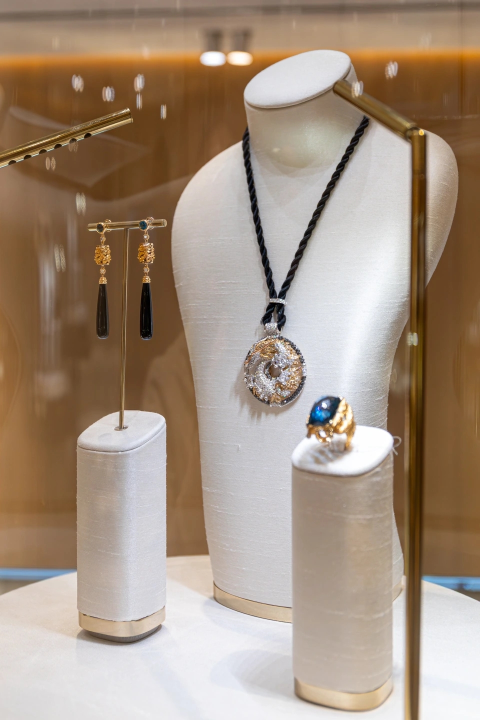 Colección de joyas en la que se muestra pendientes anillo y colgante con piedras preciosas engarzadas en vitrina de cristal con iluminación cálida
