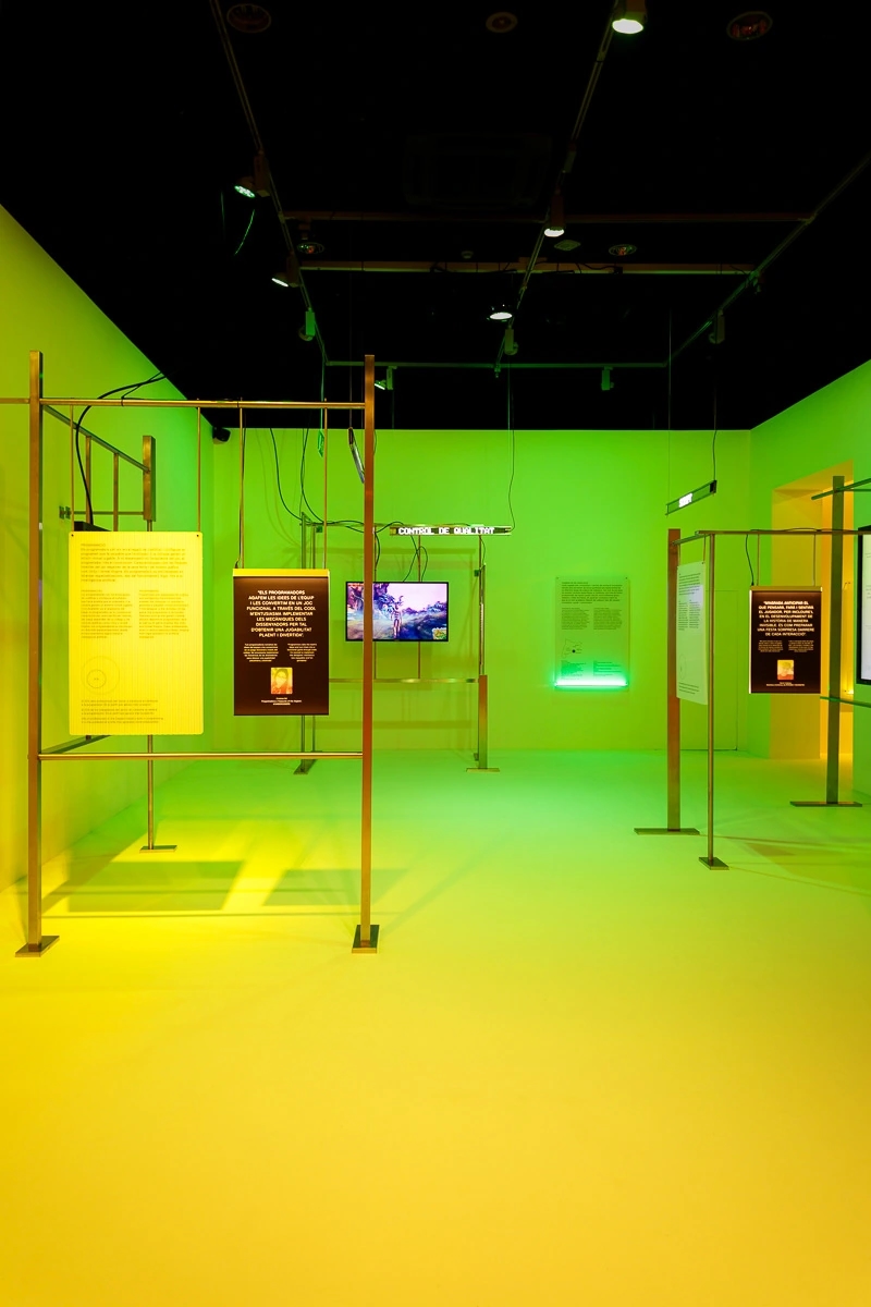 Fotografia de la escenografia de la exposición de Nueva pantalla, el videojuego en Cataluña. Fondo verde y muchas actividades tecnológicas.