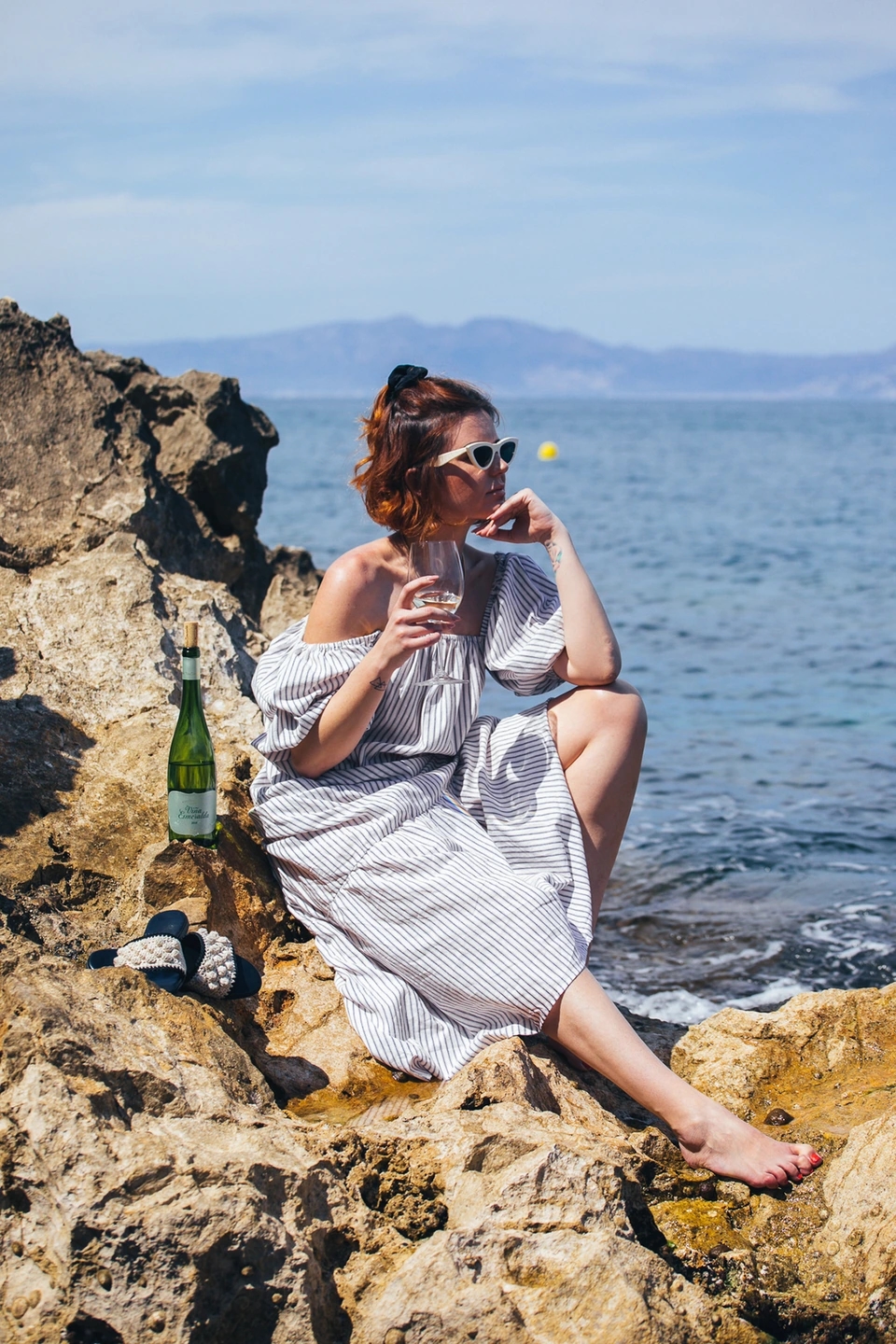 Mujer con botella de Viña Esmeralda mediterranean descansando en las rocas del mediterráneo.