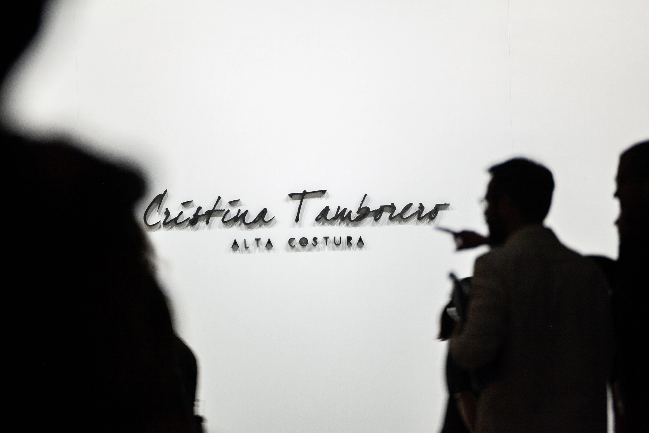 Escenario del desfile de Cristina Tamborero para la Barcelona Bridal Fashion Week. Personas desenfocadas señalando el cartel.