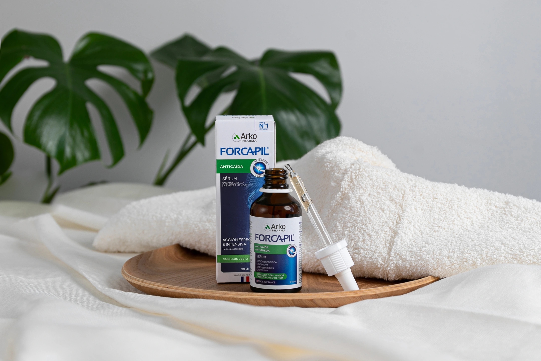 Sérum anticaída con una toalla y una planta de fondo, producto de la marca Forcapil, producto de la farmacéutica Arkopharma para una sesión fotográfica creativa en Madrid.