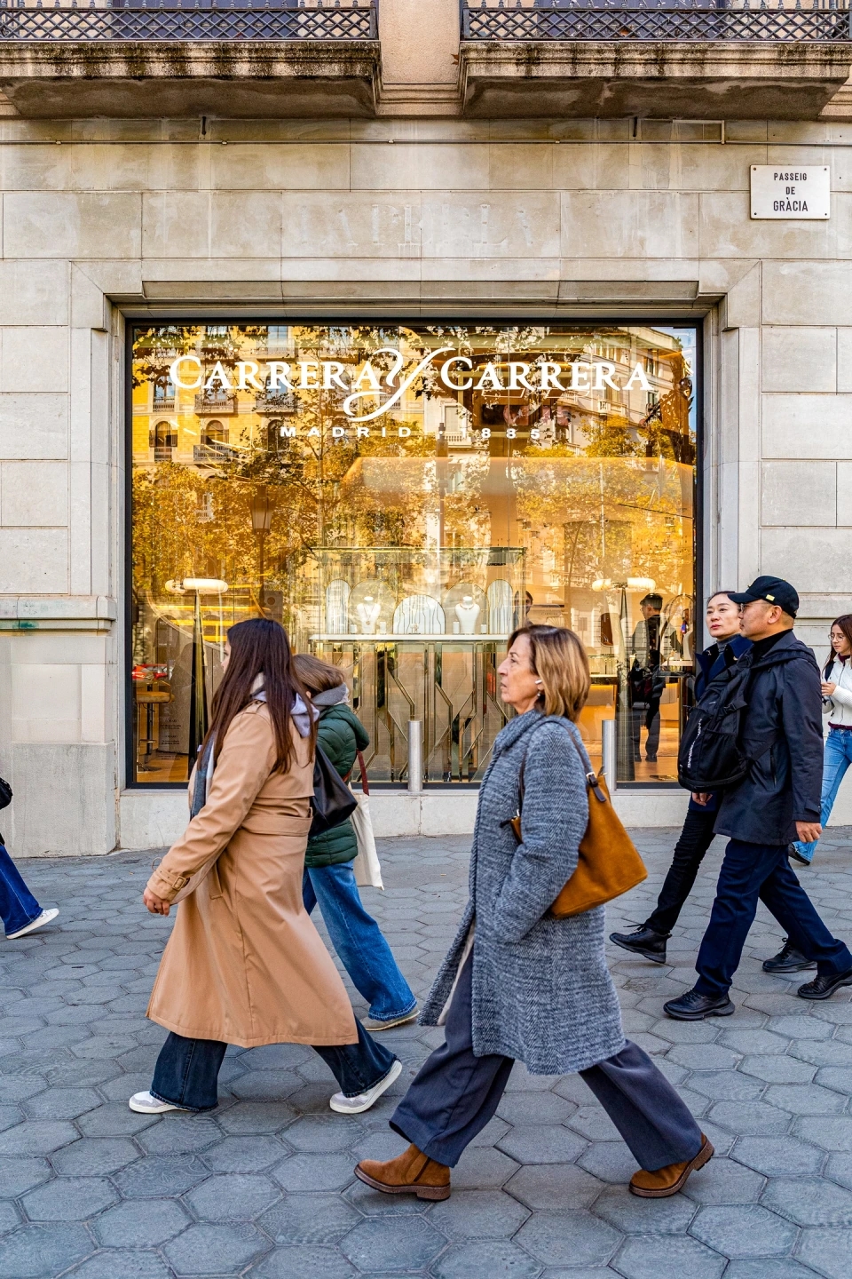 Gente paseando delante de la tienda de carreraycarrera situada en paseo de gracia escaparate dominado por luz cálida y mostrando varias colecciónes de joyas de la propia joyería