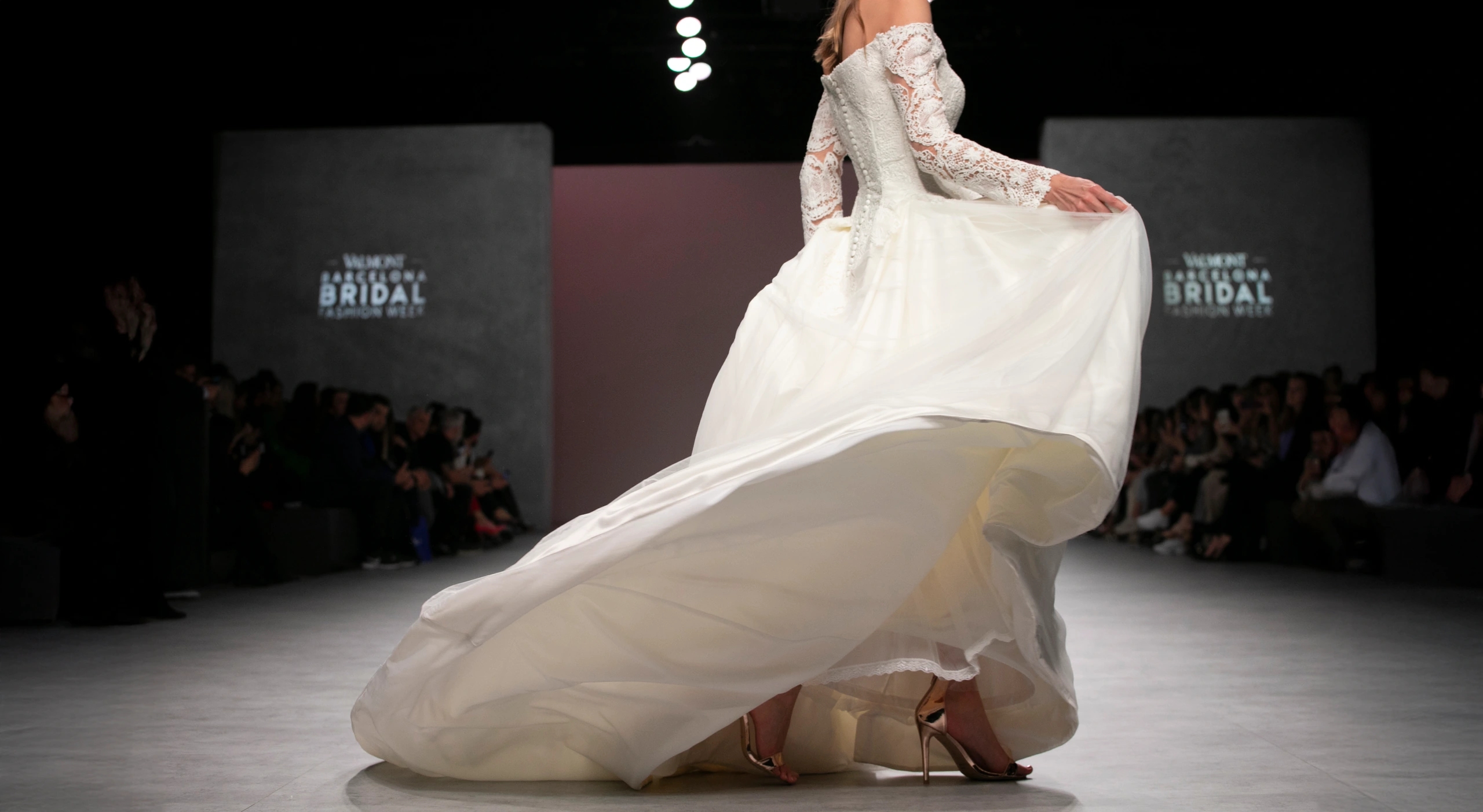 Modelo con vestido de novia vaporoso girando en la pasarela del desfile de María Salas para la Barcelona Bridal Fashion Week.