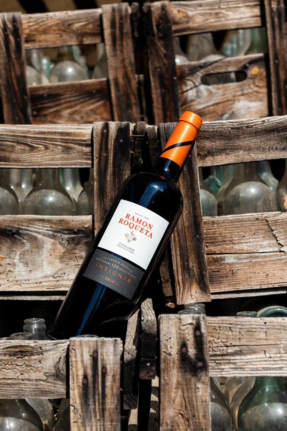 Botella de vino Ramon Roqueta apoyada en cajas de botellas de en el viñedo de las bodegas Ramon Roqueta en DO Bages, Cataluña al atardecer.