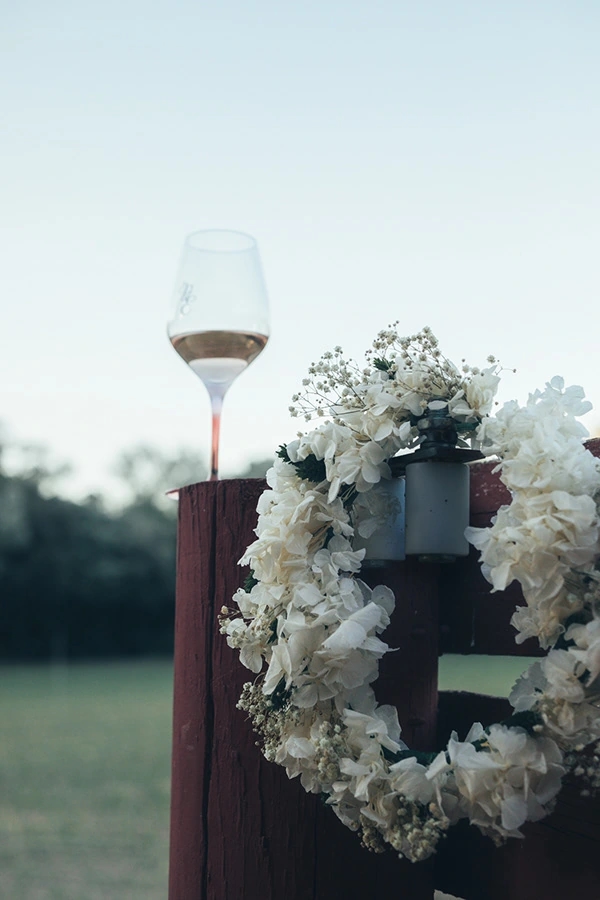 copa de vino rosado Viña Esmeralda mediterranean encima de un poste de establo con una tiara de flores blancas colgando. Viña Esmeralda mediterranean.